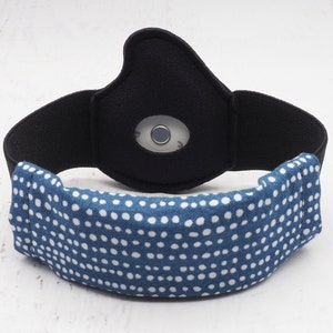 May include: A black sleep mask with a blue and white polka dot fabric covering the front. The mask has a small, round, clear window with a silver sensor inside.