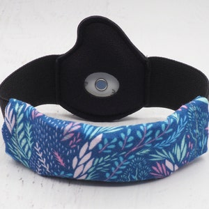 Op de afbeelding: Een zwart hoofdband met een blauw en wit bloemenpatroon. Het hoofdband heeft een klein, rond, transparant venster in het midden.