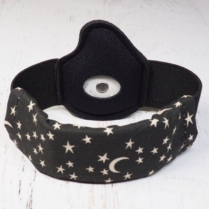 Op de afbeelding: Zwart hoofdband met een wit halve maan en sterrenpatroon. Het hoofdband heeft een zwart elastisch band en een zwart gevoerd gedeelte met een klein rond wit licht.