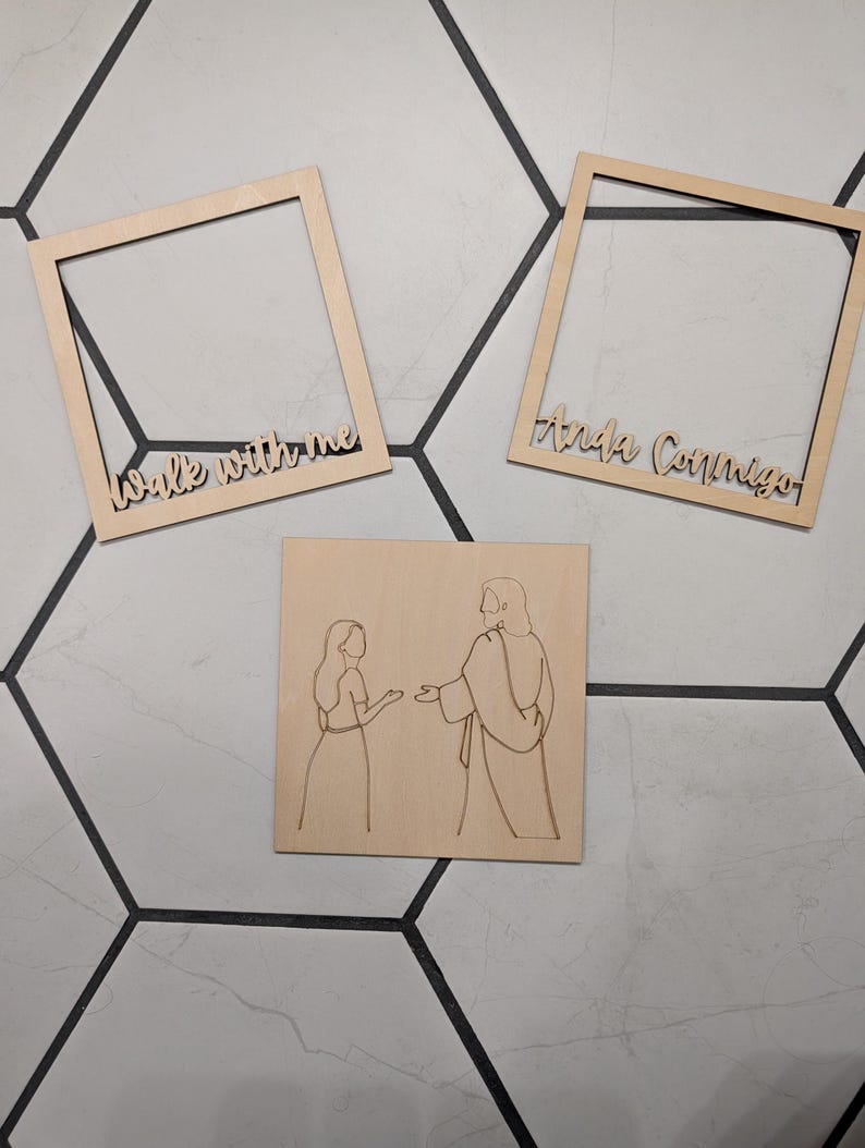 Pode incluir: Dois quadros quadrados de madeira clara e uma placa quadrada de madeira. Um quadro apresenta o texto "Walk with me" e o outro "Anda Conmigo". A placa exibe uma ilustra&ccedil;&atilde;o de linhas de uma pessoa diante de uma figura.
