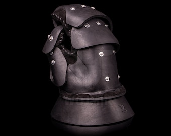 May include: Black leather gauntlet with metal rivets and a padded cuff. The gauntlet is designed for protection and has a textured surface.