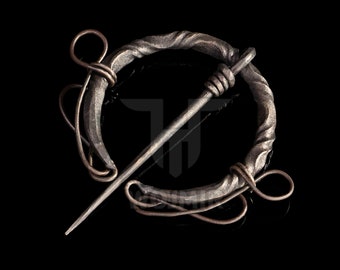 May include: A silver-toned metal brooch with a twisted circular design and a long pin. The pin is attached to the brooch with a small loop.