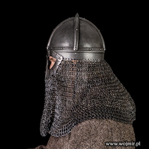 Puede incluir: Un primer plano de un casco medieval con una cota de malla. El casco est&aacute; hecho de metal y tiene una punta puntiaguda. La cota de malla est&aacute; hecha de anillos de metal y cubre la cara y el cuello del usuario.