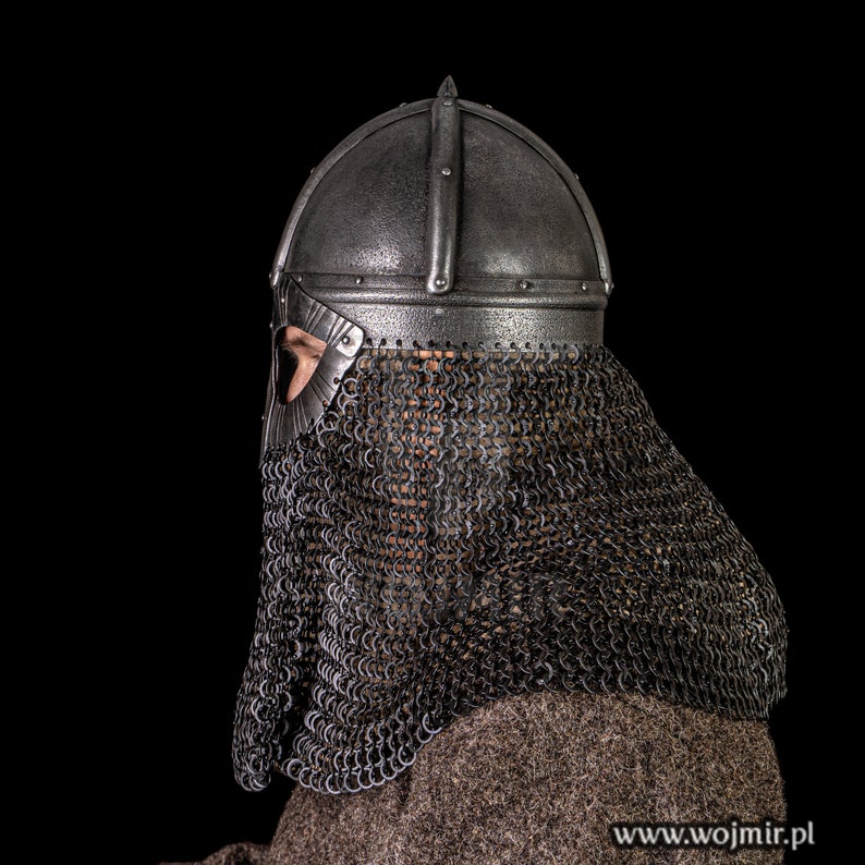 Puede incluir: Un primer plano de un casco medieval con una cota de malla. El casco est&aacute; hecho de metal y tiene una punta puntiaguda. La cota de malla est&aacute; hecha de anillos de metal y cubre la cara y el cuello del usuario.