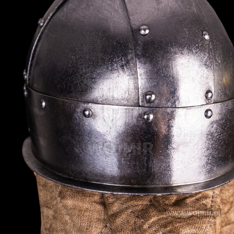 Puede incluir: Un casco plateado con remaches y un forro de tela marr&oacute;n. El casco est&aacute; hecho de metal y tiene una forma redondeada.