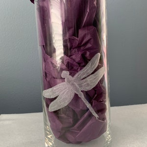 May include: A clear glass vase with an etched dragonfly design. The vase is filled with purple tissue paper.