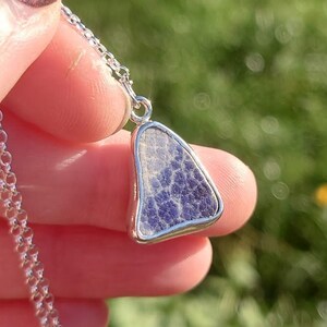 May include: A silver chain necklace with a pendant featuring a triangular piece of purple and white sea glass.