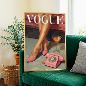 May include: A framed wall art print featuring the word VOGUE in white capital letters. The illustration depicts a pair of legs in pink high-heeled pumps, a martini glass with an orange drink, and a vintage pink rotary telephone on a floor.