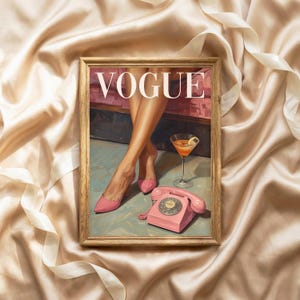May include: A framed print featuring the word VOGUE in white capital letters. The artwork depicts a pair of legs in pink high-heeled shoes, a martini glass with an orange liquid, and a pink rotary telephone on a light blue floor surface.