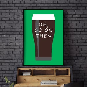 Puede incluir: Un cuadro enmarcado con un fondo verde que representa una pinta de cerveza oscura. El vaso est&aacute; lleno de un l&iacute;quido marr&oacute;n oscuro y coronado con espuma blanca. Las palabras "OH, GO ON THEN" est&aacute;n impresas en blanco en el vaso.