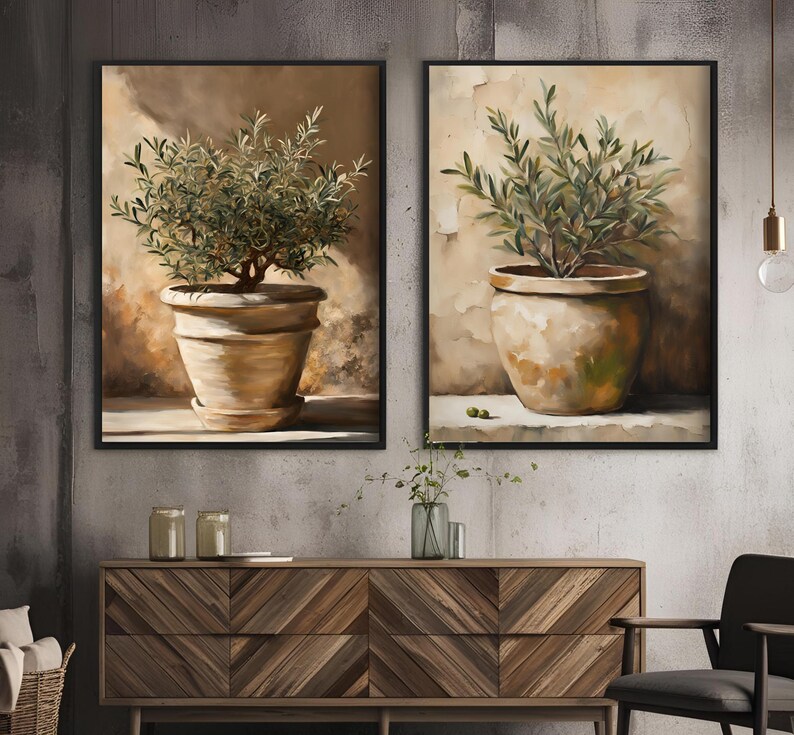 May include: Two framed paintings of olive trees in terracotta pots against a beige background. The paintings are in black frames and are hung on a gray wall.