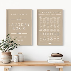 Op de afbeelding: Twee ingelijste borden voor de wasruimte met beige achtergronden. Op één bord staat "LAUNDRY ROOM" met "OPEN 24 HOURS" en "SELF SERVICE" erboven en eronder. Het andere bord is een wasgids met wasvoorschriften.