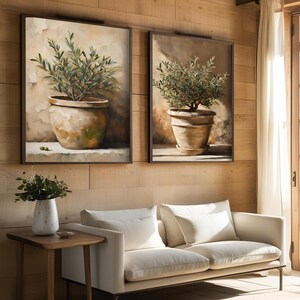 May include: Two framed paintings of olive trees in terracotta pots, hanging on a wood wall above a white sofa.