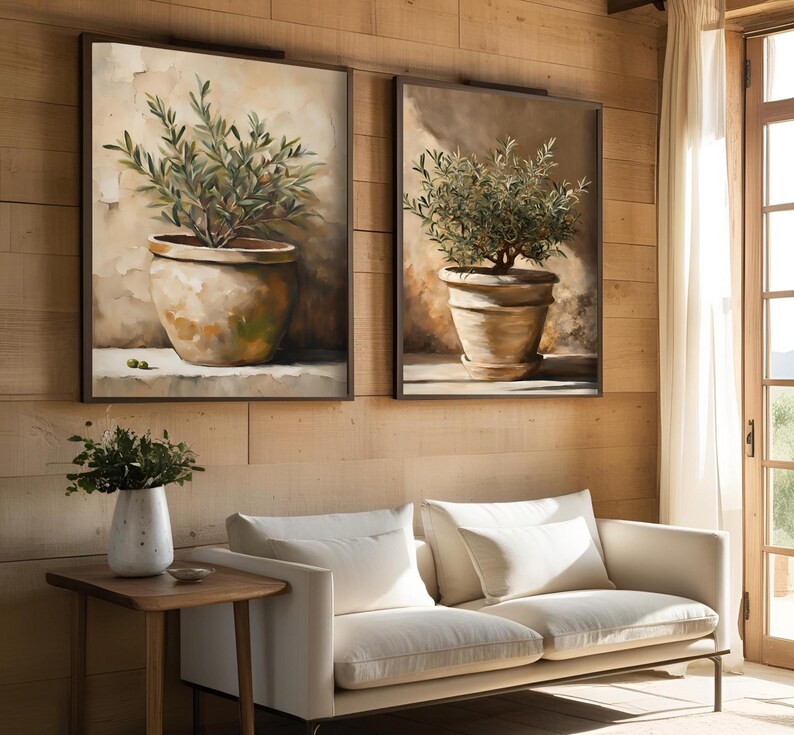 May include: Two framed paintings of olive trees in terracotta pots, hanging on a wood wall above a white sofa.