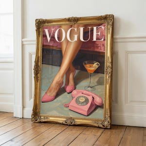 May include: A framed wall art print featuring a vintage Vogue magazine cover illustration. The artwork depicts a pair of legs in pink high-heeled shoes, a cocktail glass with an orange drink, and a pink rotary telephone on a light blue floor.