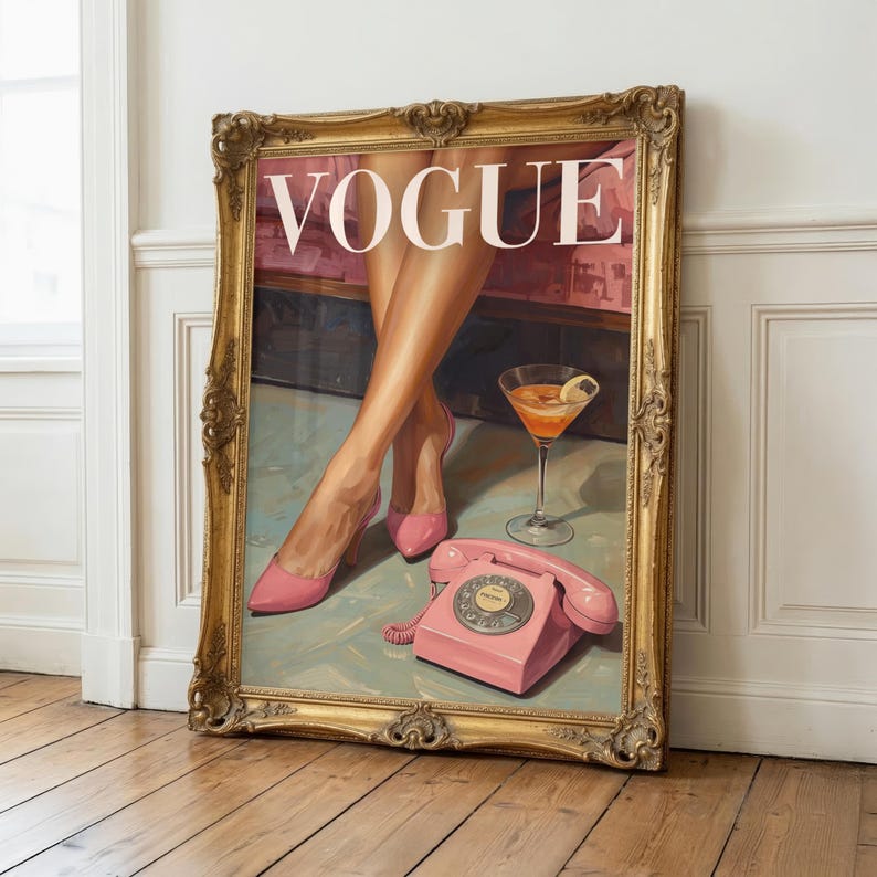 May include: A framed wall art print featuring a vintage Vogue magazine cover illustration. The artwork depicts a pair of legs in pink high-heeled shoes, a cocktail glass with an orange drink, and a pink rotary telephone on a light blue floor.