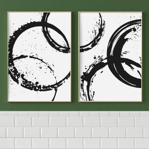 May include: Two black and white abstract art prints with a circular design. The prints are framed in a light wood frame.
