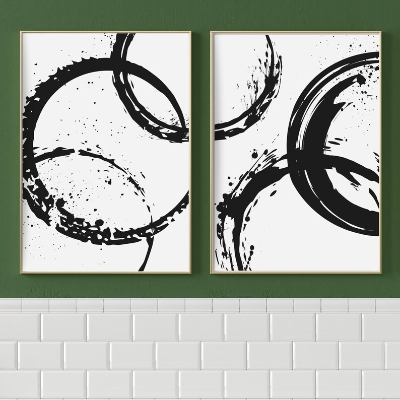 May include: Two black and white abstract art prints with a circular design. The prints are framed in a light wood frame.
