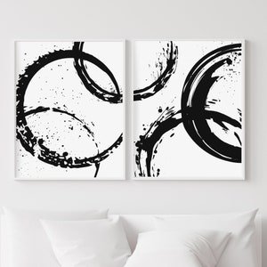 May include: Two black and white abstract art prints with a circular design. The prints are framed in white and have a white background.