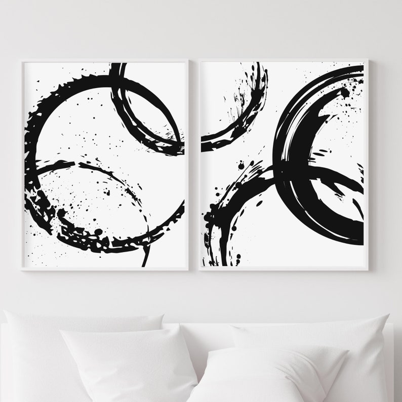 May include: Two black and white abstract art prints with a circular design. The prints are framed in white and have a white background.