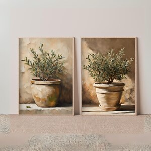 May include: Two framed paintings of olive trees in terracotta pots. The paintings are set against a light brown background.