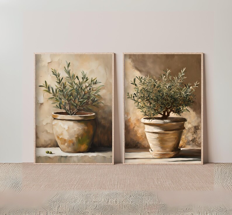 May include: Two framed paintings of olive trees in terracotta pots. The paintings are set against a light brown background.
