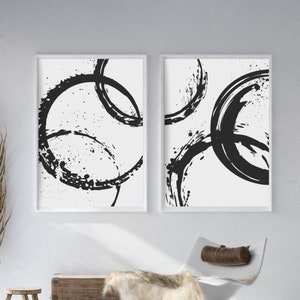 May include: Two black and white abstract art prints with a circular design. The prints are framed in white and have a white background.