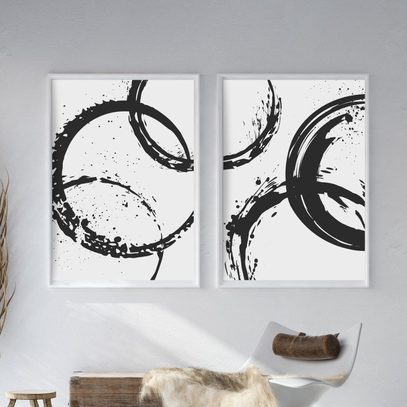 May include: Two black and white abstract art prints with a circular design. The prints are framed in white and have a white background.