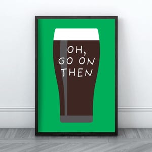 Puede incluir: Un p&oacute;ster enmarcado que muestra una pinta de cerveza oscura con espuma blanca sobre un fondo verde. Las palabras "OH, GO ON THEN" est&aacute;n escritas en blanco sobre el vaso. El p&oacute;ster est&aacute; en un marco negro.