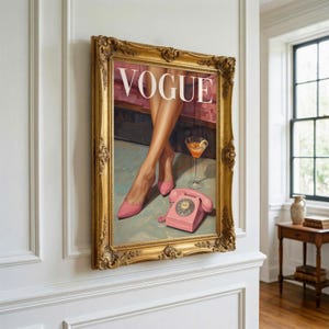 May include: A framed wall art print featuring the word VOGUE in white capital letters. The illustration depicts a pair of legs in pink high-heeled shoes, a cocktail glass, and a pink rotary telephone on a light blue surface with a gold frame.