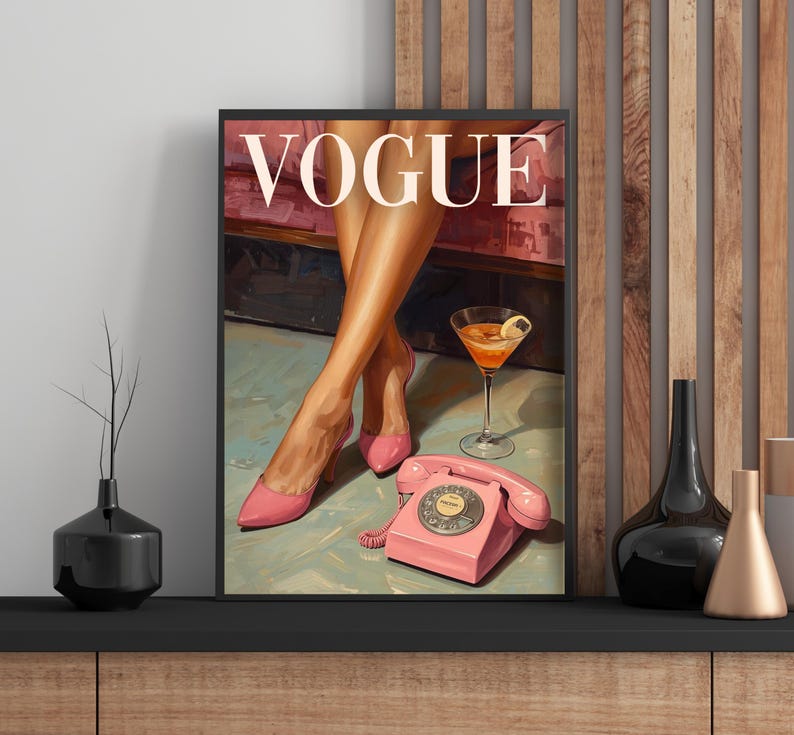 May include: A framed wall art print featuring the word VOGUE in white capital letters. The illustration depicts a pair of legs in pink high-heeled shoes, a pink rotary telephone, and a cocktail glass with a lemon slice on a light surface.