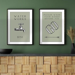 Pode incluir: Duas impressões artísticas emolduradas com molduras pretas. A impressão da esquerda diz "WATER WORKS" acima de uma ilustração de torneira e "$150" abaixo. A impressão da direita diz "PLEASE WASH YOUR HANDS BEFORE YOU GO" com uma seta.