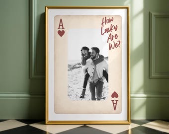 May include: A framed print resembling an Ace of Hearts playing card. The card features a black and white photo of a couple, with the text "How Lucky Are We?" in red script. The frame is gold.