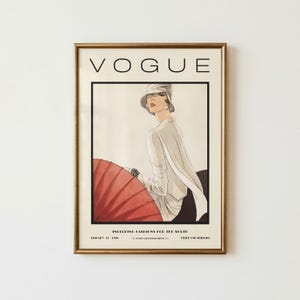 Może przedstawiać: Oprawiony wydruk okładki magazynu Vogue ze stycznia 1929 roku z ilustracją osoby w białym topie i kapeluszu, trzymającej duży czerwony parasol. Tekst głosi VOGUE, INCLUDING FASHIONS FOR THE SOUTH, JANUARY 1929, PRICE ONE SHILLING.