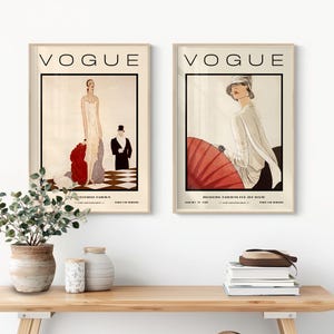 Może przedstawiać: Dwie oprawione grafiki z okładkami magazynu Vogue. Lewa grafika przedstawia osobę w białej sukni z czerwoną narzutką oraz osobę w smokingu na szachownicowej podłodze. Prawa grafika przedstawia osobę w białym kapeluszu i koszuli trzymającą czerwony parasol przeciwsłoneczny.