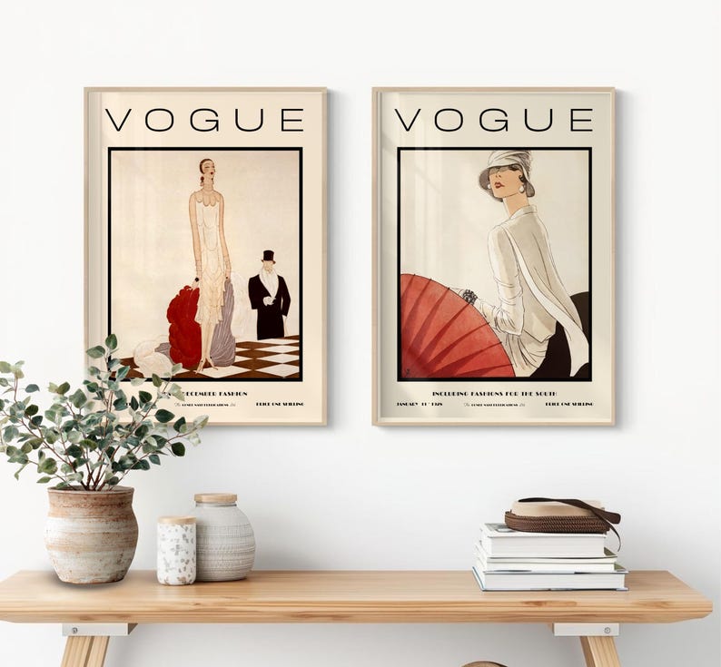 Może przedstawiać: Dwie oprawione grafiki z okładkami magazynu Vogue. Lewa grafika przedstawia osobę w białej sukni z czerwoną narzutką oraz osobę w smokingu na szachownicowej podłodze. Prawa grafika przedstawia osobę w białym kapeluszu i koszuli trzymającą czerwony parasol przeciwsłoneczny.