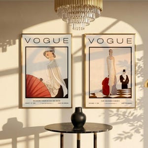 Może przedstawiać: Dwie oprawione grafiki z okładkami magazynu Vogue z ilustracjami mody vintage. Lewa grafika przedstawia osobę w białym stroju z czerwonym parasolem. Prawa grafika przedstawia osobę w białej sukni oraz osobę w czarnym garniturze.