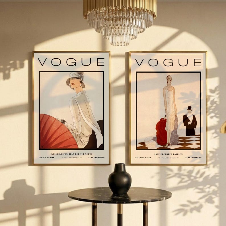 Może przedstawiać: Dwie oprawione grafiki z okładkami magazynu Vogue z ilustracjami mody vintage. Lewa grafika przedstawia osobę w białym stroju z czerwonym parasolem. Prawa grafika przedstawia osobę w białej sukni oraz osobę w czarnym garniturze.