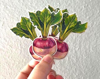 May include: A die-cut sticker featuring a cluster of three turnips with vibrant purple and white rounded roots and lush, detailed green leafy tops. The illustration uses bold colors and clear outlines to define the vegetable shapes.
