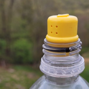 May include: A clear plastic bottle with a yellow lid. The lid has three holes in it.