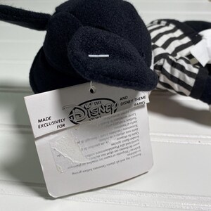 May include: A black plush toy with a white and black striped outfit. The toy has a tag that reads "MADE EXCLUSIVELY FOR THE DISNEY STORE AND DISNEY THEME PARKS".