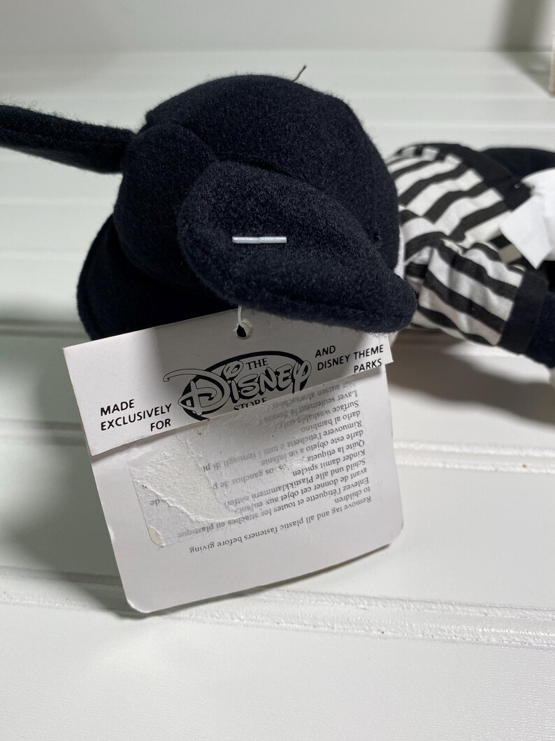 May include: A black plush toy with a white and black striped outfit. The toy has a tag that reads "MADE EXCLUSIVELY FOR THE DISNEY STORE AND DISNEY THEME PARKS".
