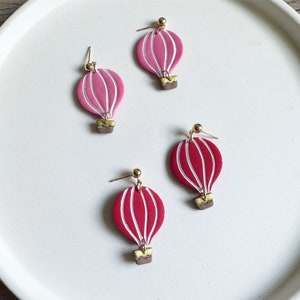 May include: Four pairs of pink and red hot air balloon earrings. The earrings are made of polymer clay and have a gold-colored wire.