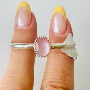 May include: A silver ring with a pink oval stone and a silver arrow design.