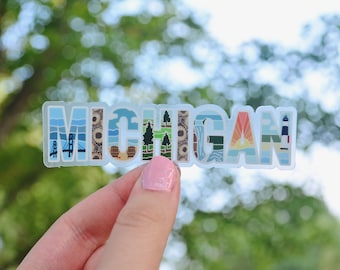 Puede incluir: Una pegatina transparente con la palabra "MICHIGAN" escrita en letras de colores. Cada letra está llena de una ilustración diferente que representa varios monumentos y atracciones de Michigan.
