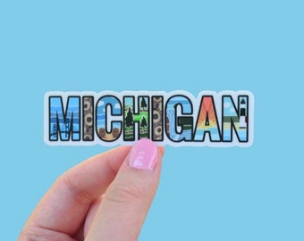 May include: A white sticker with the word "MICHIGAN" in blue letters. Each letter is filled with a different image representing a place or landmark in Michigan.