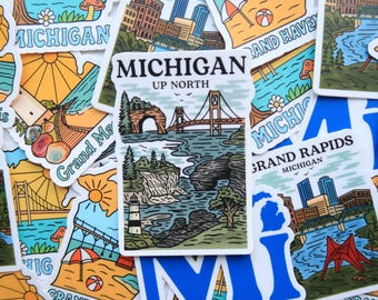 May include: A collection of colorful Michigan-themed stickers. The stickers feature illustrations of bridges, lighthouses, and cityscapes, with text that reads "Michigan" and "Grand Rapids". The stickers are in various shapes and sizes, with a mix of blue, orange, and green.