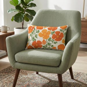 Pu&ograve; includere: Un cuscino rettangolare con un motivo floreale di papaveri arancioni e foglie verdi poggia su una poltrona verde chiaro. La sedia ha gambe in legno ed &egrave; posizionata su un tappeto fantasia. Una pianta in vaso &egrave; visibile sullo sfondo.