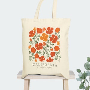 May include: A beige tote bag with a design of orange and yellow California poppies on a white background. The text "CALIFORNIA" and "CALIFORNIA POPPY" is printed in black at the bottom of the bag.