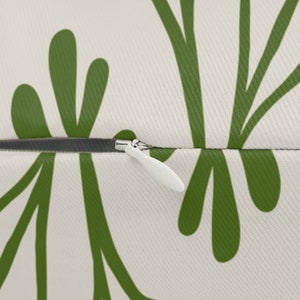 Pu&ograve; includere: Primo piano di un cuscino bianco con un motivo floreale verde. Il cuscino ha una cerniera bianca. Il design verde &egrave; un motivo ripetuto di foglie e steli stilizzati.